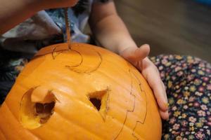 preparação do dia das bruxas. criança esculpindo abóbora em jack-o-lanterna enquanto está sentado no chão da casa. foto