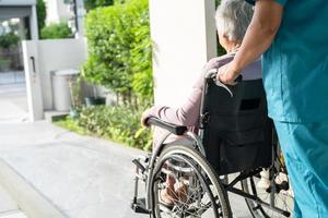 cuidador, ajuda e cuidado paciente idoso asiático ou idosa senhora sentada em uma cadeira de rodas na rampa de um hospital de enfermagem, conceito médico forte e saudável foto