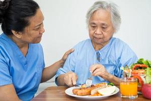 paciente asiático sênior ou idosa idosa comendo alimentos saudáveis de vegetais de café da manhã com esperança e feliz enquanto está sentado e com fome na cama no hospital. foto