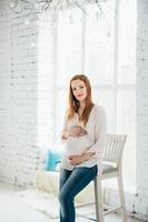 uma garota ruiva grávida em uma blusa leve e jeans azul foto