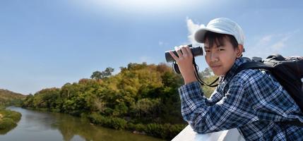 meninos asiáticos usando binóculos para observar pássaros em árvores e pescar no rio no parque nacional local durante o acampamento de verão, ideia para aprender criaturas e animais selvagens e insetos fora da sala de aula. foto