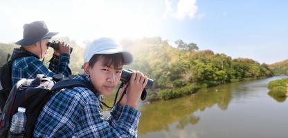 meninos asiáticos usando binóculos para observar pássaros em árvores e pescar no rio no parque nacional local durante o acampamento de verão, ideia para aprender criaturas e animais selvagens e insetos fora da sala de aula. foto