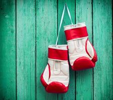 par de luvas de boxe vermelhas penduradas em um prego em um fundo de superfície de madeira verde foto