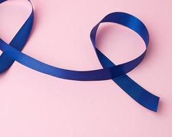 fita de seda azul escura torcida em loops em um fundo rosa foto