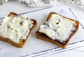 pão torrado com requeijão macio em uma placa de madeira branca foto