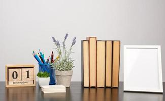 moldura branca vazia, pilha de livros e um pote de cultivo de lavanda em uma mesa preta foto