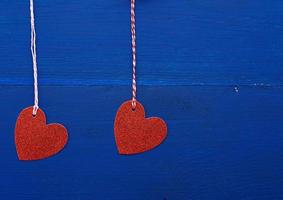 corações decorativos brilhantes de papel vermelho pendurado em uma corda em um fundo de madeira azul escuro foto