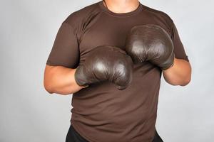 jovem fica em um rack de boxe, usando luvas de boxe marrons muito antigas em suas mãos foto