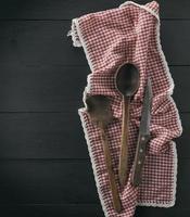velha colher de pau, escápula e faca em uma toalha têxtil vermelha foto