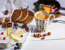 café preto com espuma marrom, atrás de um queijo camembert redondo foto