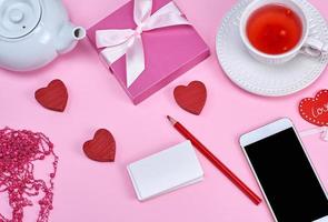 cartões de visita vazios de papel branco, smartphone e chá de ervas em um fundo rosa foto