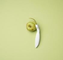 faca de plástico para descascar legumes, frutas e uma maçã verde sobre fundo verde foto