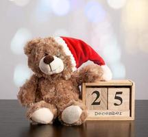 ursinho marrom com chapéu vermelho, calendário de mesa de madeira com a data de 25 de dezembro foto