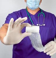 médico de uniforme azul e luvas de látex segurando bandagem de curativo de gaze estéril branca foto