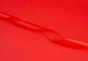fita brilhante de seda vermelha torcida em um fundo vermelho, elemento de design festivo foto