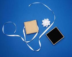 caixa quadrada com um presente amarrado com uma fita branca com um laço em um fundo azul clássico, vista superior foto