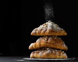 uma pilha de croissants assados polvilhados com açúcar de confeiteiro em um fundo preto foto