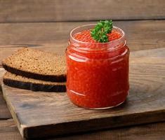 frasco de vidro cheio com caviar vermelho em uma mesa de madeira marrom, café da manhã foto