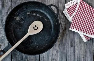 frigideira de ferro fundido preto com uma colher de pau em uma superfície de madeira cinza foto