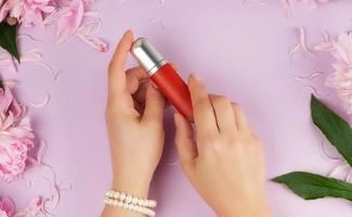mãos femininas com pele clara e lisa mantêm batom vermelho líquido em um tubo foto