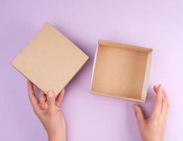 menina abre uma caixa quadrada marrom em um fundo roxo foto