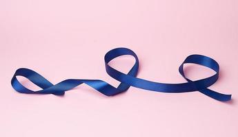 fita de seda azul escura torcida em loops em um fundo rosa foto