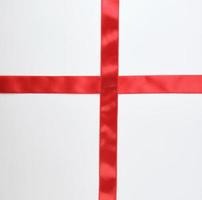 cruz de fita de cetim vermelha para cruzar no fundo branco foto