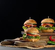 cheeseburger com rissol de carne grelhada, queijo cheddar, tomate e alface em uma placa de madeira, fundo preto foto