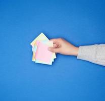 mão feminina e muitos adesivos multicoloridos de papel vazio em um fundo azul foto