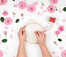 duas mãos femininas segurando um aro redondo de madeira e um fio vermelho com uma agulha foto