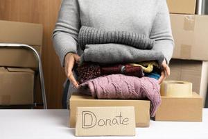 mulher de suéter cinza está embalando roupas em uma caixa, o conceito de assistência e voluntariado foto