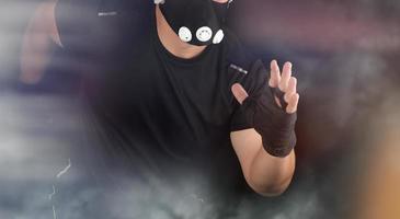 atleta adulto em um uniforme preto, máscara e corre e rompe uma cortina de fumaça foto