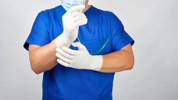 médico de uniforme azul coloca nas mãos luvas brancas de látex estéreis foto