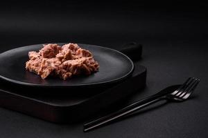 deliciosa carne de atum enlatada em uma placa de cerâmica preta sobre um fundo escuro de concreto foto
