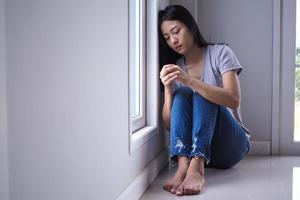 uma mulher asiática estava tristemente sentada perto da janela da sala. sentindo-se triste e solitário. foto