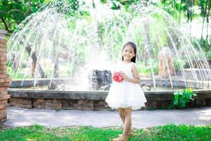 menina asiática linda em um vestido branco segurando um presente vermelho no parque foto