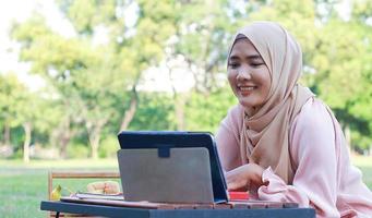 linda garota muçulmana sentada alegremente no parque. mulher muçulmana sorrindo no gramado do jardim. conceito de estilo de vida de uma mulher moderna confiante foto