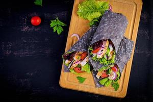 tortilla com choco adicionado de tinta envolve com frango e legumes em fundo preto. burrito de frango, comida mexicana. vista do topo foto