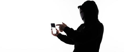 hacker anônimo e máscara facial com smartphone na mão. homem de camisa de capuz preto segurando e usando o celular em fundo branco. represente o hacking de dados de crimes cibernéticos ou o roubo do conceito de dados pessoais foto