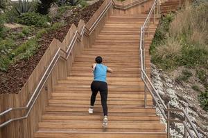mulher correndo com uma camisa azul e subindo uma escada de madeira