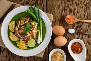 Pad thai com limão, ovos e temperos em uma mesa de madeira foto