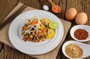 Pad thai com limão, ovos e temperos em uma mesa de madeira foto