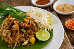 Pad thai com limão, ovos e temperos em uma mesa de madeira foto