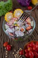 salada de frutas e vegetais em uma tigela de vidro na mesa de madeira foto