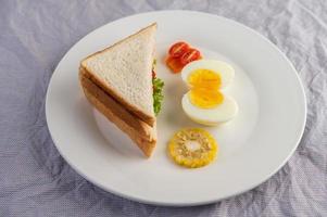 Ovos cozidos, milho, sanduíche de tomate em um prato branco