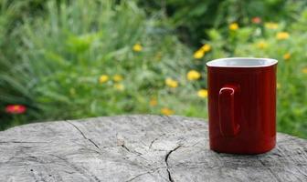 caneca vermelha de café na mesa de madeira contra verde desfocado foto