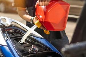 homem enche o tanque de gasolina da motocicleta a partir de uma vasilha vermelha ou lata de combustível de plástico conceito de motocicleta de reparo de manutenção, foco seletivo foto