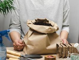 uma mulher com roupas cinza segura um saco de terra para plantar sementes em copos de papel. passatempo e lazer foto