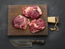 faca e pedaço cru de ribeye de carne em uma mesa preta, vista superior foto