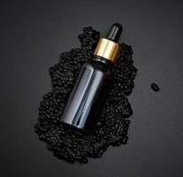 garrafa de vidro com uma pipeta encontra-se em um monte de caviar preto, fundo preto. cômico natural. marca do produto, vista superior foto